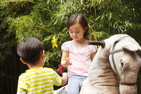 动物幼儿园摄影照片_可爱的小女孩在骑摇摆木马