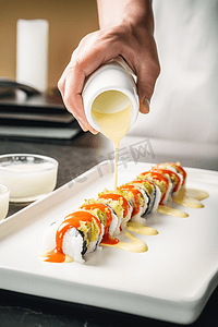 美食酒店摄影照片_酒店或餐厅的厨师用瓶装日本蛋黄酱装饰美味的面包卷。准备寿司套装。只手
