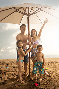 遮阳伞女孩摄影照片_海滩上躲在遮阳伞下的四口之家