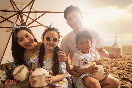 幸福的四口之家坐在沙滩上喝椰汁