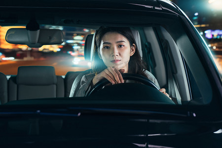 车窗车灯摄影照片_夜晚驾驶汽车的青年女人