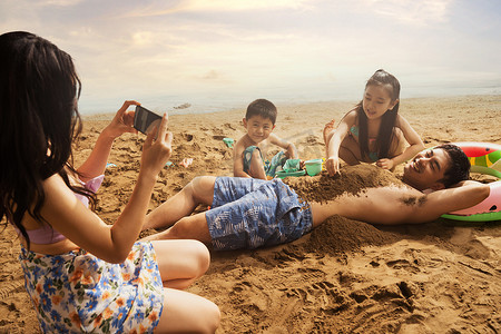 游泳圈的男孩摄影照片_沙滩上青年女人为丈夫孩子拍照