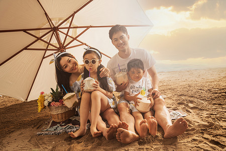 幸福的四口之家坐在沙滩上喝椰汁