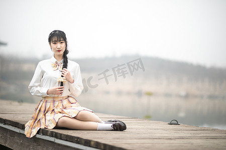 穿着jk制服的女孩坐在公园湖边的木桥上