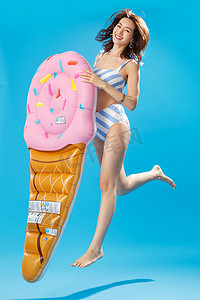 拿着冰淇淋形状的浮排跳跃的比基尼美女