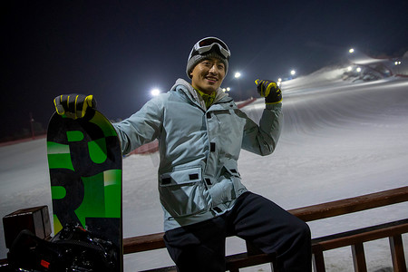 夜晚青年男人坐在滑雪场内的护栏上
