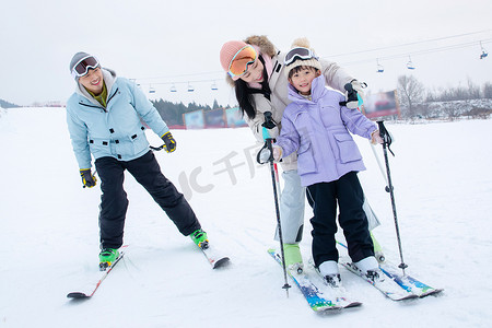 儿童拿的动作摄影照片_滑雪场上教女儿滑雪的一家三口