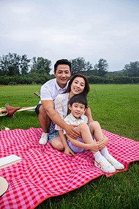 坐在野餐垫上摄影照片_幸福的一家三口坐在野餐垫上