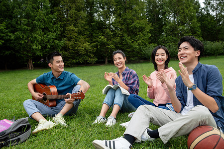 坐弹吉他摄影照片_快乐的大学生在草地上弹吉他唱歌