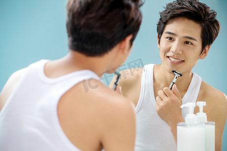 刮胡刀海报摄影照片_青年男人对着镜子刮胡子