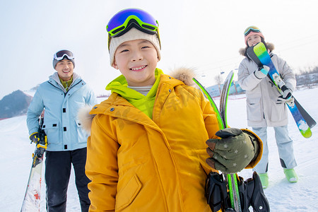 雪场上拿着滑雪板的一家三口