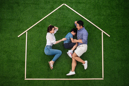 房地产轮廓摄影照片_快乐的一家三口躺在草地上的房子轮廓里玩耍