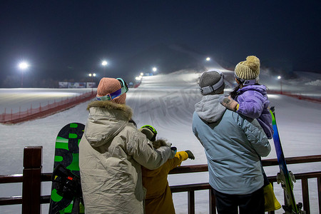 冬天的夜景摄影照片_滑雪场看夜景的一家四口的背影