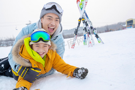 雪地打滚摄影照片_滑雪场内抱在一起打滚的快乐父子