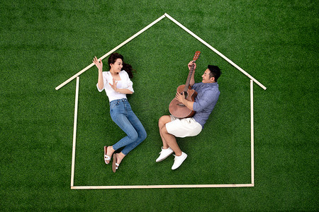 房地产轮廓摄影照片_青年伴侣躺在草地上的房子轮廓里唱歌跳舞