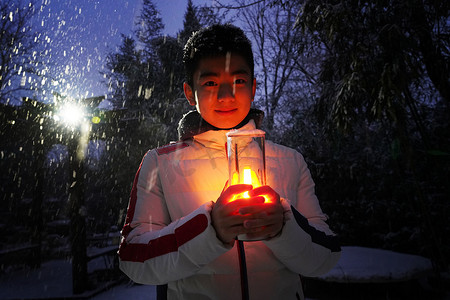 夜晚雪景摄影照片_男孩在院子里手捧小台灯