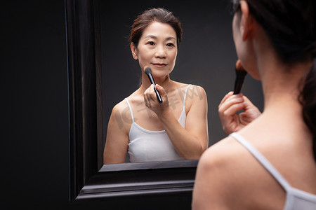 亚洲成熟护肤摄影照片_对着镜子化妆的成熟女人