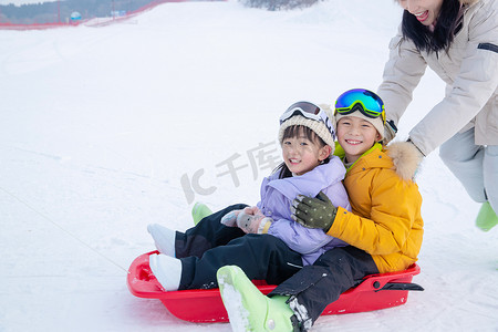 妈妈儿子奔跑摄影照片_雪场上妈妈推着坐在雪上滑板的孩子们