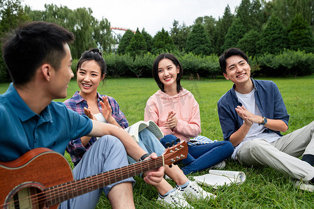 坐弹吉他摄影照片_快乐的大学生在草地上弹吉他唱歌