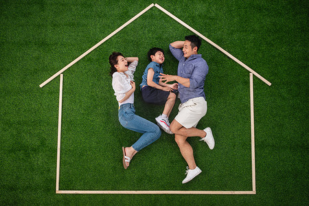 快乐的一家三口躺在草地上的房子轮廓里玩耍