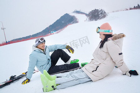 雪地玩耍人物摄影照片_快乐的青年伴侣坐在雪地上闲聊