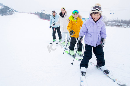 雪地玩耍人物摄影照片_滑雪场内排成一排滑雪的年轻家庭
