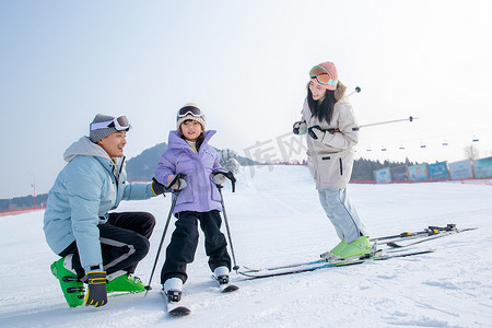 滑雪场上教女儿滑雪的一家三口