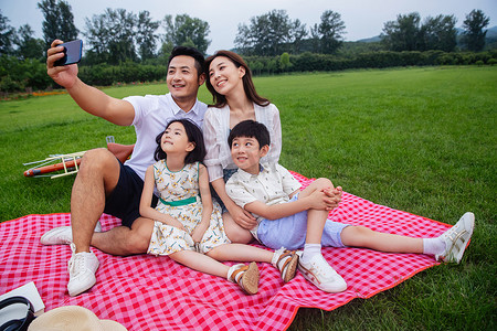 坐在野餐垫上摄影照片_幸福的一家四口坐在野餐垫上自拍
