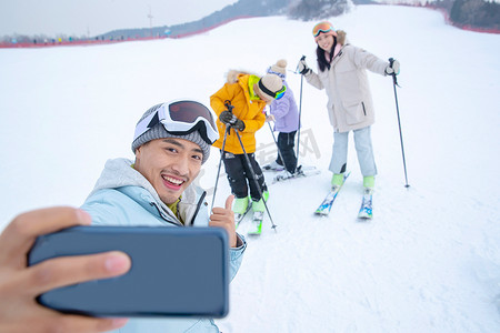 户外做运动摄影照片_滑雪场上用手机自拍的一家四口