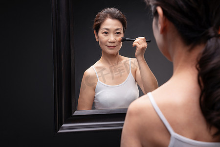 亚洲成熟护肤摄影照片_对着镜子化妆的成熟女人