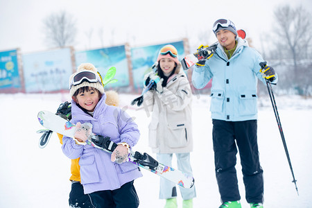 儿童滑雪摄影照片_雪场上拿着雪具去滑雪的一家四口