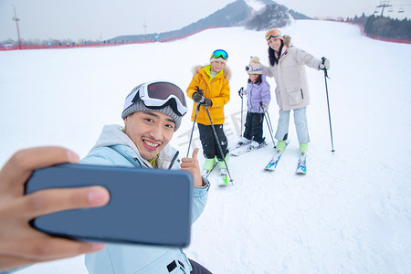 户外做运动摄影照片_滑雪场上用手机自拍的一家四口