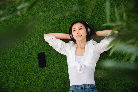 草地音乐摄影照片_躺在草地上听音乐的青年女人