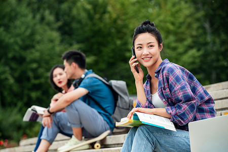 绿色校园摄影照片_快乐的大学生坐在台阶上打电话