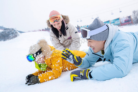 冬季亲情摄影照片_快乐的一家三口趴在雪地上玩雪