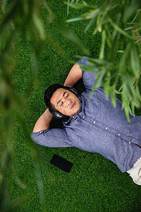 人躺在草地摄影照片_躺在草地上听音乐的青年男人