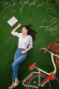 自行车青年女人摄影照片_躺在草地上享受大自然的青年女人