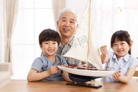 玩具帆船摄影照片_祖父陪孙辈在客厅玩耍