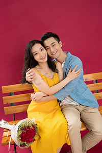 抱着玫瑰花摄影照片_幸福的青年伴侣坐在长椅上