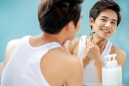 刮胡刀海报摄影照片_青年男人对着镜子刮胡子