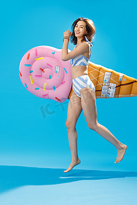 清爽一夏天摄影照片_抱着冰淇淋形状的浮排跳跃的比基尼美女