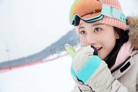 羽绒服衣服摄影照片_滑雪场上对着手哈气的青年女人