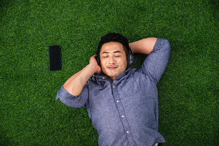 草地音乐摄影照片_青年男人躺在草地上听音乐