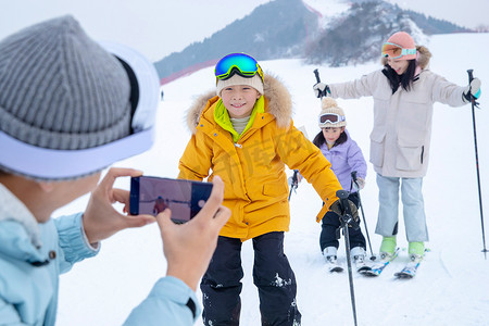 滑手机屏幕摄影照片_滑雪场上父亲用手机给孩子们和妻子拍照