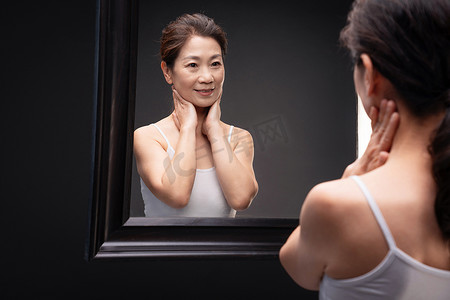 漂亮的中老年女性对着镜子做颈部护理