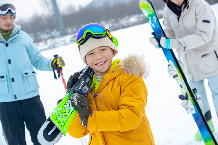 雪地玩耍人物摄影照片_雪场上拿着滑雪板的一家三口