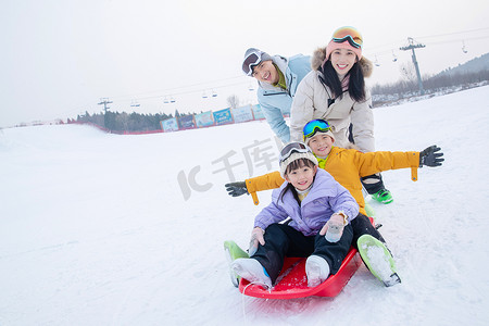 滑雪场上父母推着坐在雪上滑板的孩子们