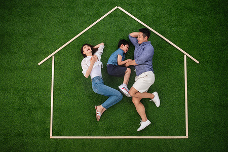 快乐的一家三口躺在草地上的房子轮廓里玩耍