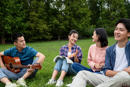 坐弹吉他摄影照片_快乐的大学生在草地上弹吉他唱歌