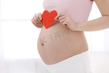 剪纸爱心摄影照片_孕妇拿着心形剪纸放在肚子上